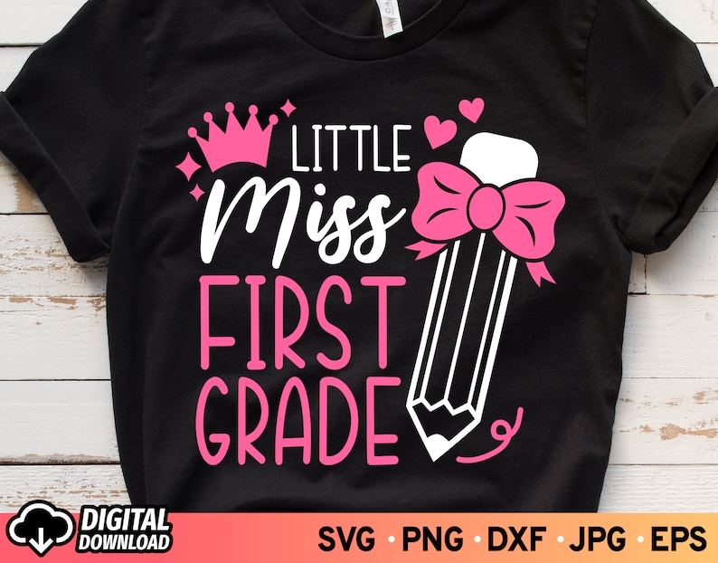 May include: Black t-shirt with a pink crown, hearts, and a pencil with a pink bow. The text "Little Miss First Grade" is written in white.