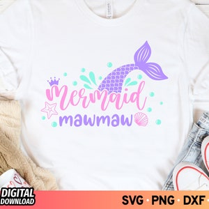 May include: A white t-shirt with a purple mermaid tail, pink crown, and the text "Mermaid Mawmaw" in pink and purple lettering. The design is surrounded by blue and green bubbles.