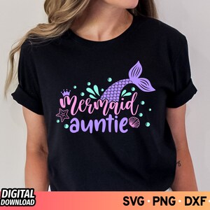 May include: Black t-shirt with a purple mermaid tail and the text "Mermaid Auntie" in pink and purple lettering. The design also includes a crown, a starfish, and seashells.