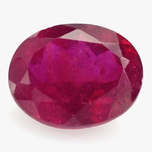 May include: A faceted, oval-shaped ruby gemstone. The gem displays a deep red hue with internal color variations. The cut reveals multiple facets, enhancing its brilliance. The ruby is set against a plain white background.