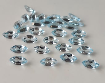 May include: A collection of marquise-cut, light blue gemstones. The gems are scattered across a white surface, each displaying facets that catch the light. The overall effect is a display of sparkling, translucent stones, perfect for jewelry making.