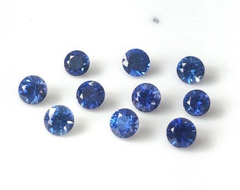 May include: A collection of ten round, faceted, deep blue gemstones. Each gem has a brilliant cut, reflecting light. The gems are scattered on a white surface, showcasing their color and clarity. Ideal for jewelry making.