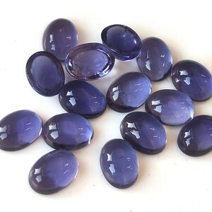 Puede incluir: Una colección de piedras preciosas ovaladas pulidas en varios tonos de púrpura. Las piedras preciosas tienen una superficie lisa y brillante, que refleja la luz. La disposición es dispersa, mostrando los diferentes tamaños y tonos de las piedras.