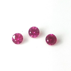 Może przedstawiać: Trzy okrągłe, fasetowane, głęboko różowe kamienie szlachetne są wyświetlane na białym tle. Kamienie mają szlif brylantowy, odbijający światło. Kamienie to prawdopodobnie rubiny, odpowiednie do biżuterii.