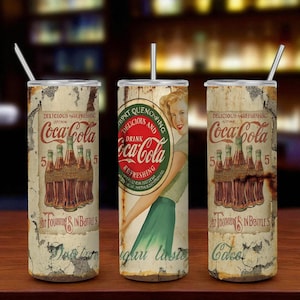 May include: Three vintage-style Coca-Cola tumblers with straws. The tumblers feature a distressed design with the Coca-Cola logo, vintage graphics, and text. The design includes a woman in a green skirt and a bottle of Coca-Cola.