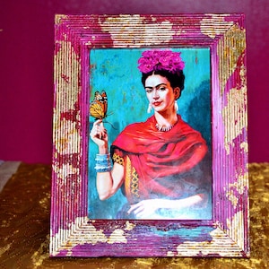 May include: A framed painting of Frida Kahlo with a butterfly on her finger. The frame is pink with gold accents.