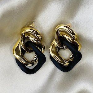 May include: A pair of gold and black statement earrings with a chain link design. The earrings are made of metal and have a geometric shape.