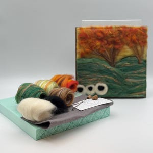 May include: A craft kit with a felted landscape scene depicting orange and green trees, green hills, and a yellow sky. The kit includes various coloured wool rolls, a needle, and a grey felt base. Two corks and two white felt eyes are also included.