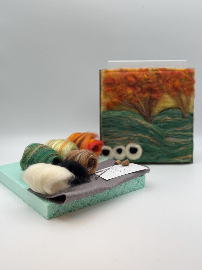 May include: A craft kit with a felted landscape scene depicting orange and green trees, green hills, and a yellow sky. The kit includes various coloured wool rolls, a needle, and a grey felt base. Two corks and two white felt eyes are also included.