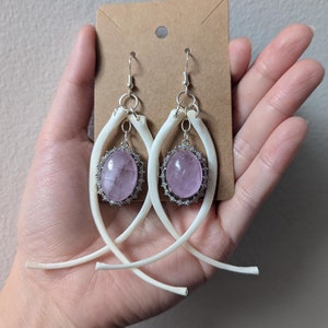 Peut inclure: Une paire de boucles d'oreilles pendantes avec un design en forme d'os et une pierre ovale rose pâle sertie dans une bélière en argent. Les boucles d'oreilles sont suspendues à des crochets en argent.
