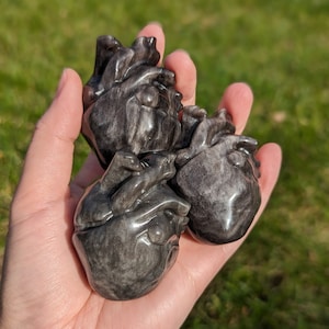 May include: Three black and grey heart-shaped stones carved from obsidian.