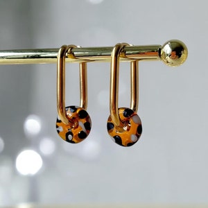 May include: A pair of gold hoop earrings with a brown and white patterned glass bead on each hoop.