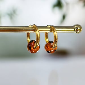 May include: A pair of gold hoop earrings with brown and black patterned glass beads.