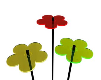 Könnte beinhalten: Drei bunte, blumenförmige Metall-Gartenpfähle mit schwarzen Metallstielen. Die Blumen sind rot, gelb und grün.