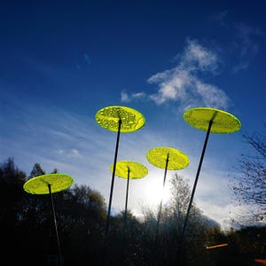 Könnte beinhalten: Fünf gelbe Glasscheiben auf Metallstangen vor einem blauen Himmel mit weißen Wolken. Die Scheiben sind leicht gewölbt und haben einen Wassertropfen-Effekt.