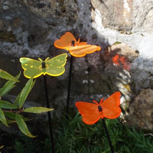 Peut inclure: Trois piquets de jardin en forme de papillon colorés, un jaune, un orange et un rouge, sont présentés dans un jardin. Les piquets sont en métal et ont une extrémité pointue pour une insertion facile dans le sol.
