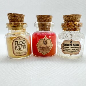 May include: Three small glass bottles with cork stoppers. The bottles contain different colored liquids and powders. The first bottle has yellow powder and the text "Floo Powder". The second bottle has red liquid and a label that says "Dragon Blood". The third bottle has a clear liquid and the text "Unicorn Blood".
