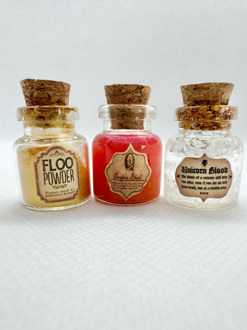 May include: Three small glass bottles with cork stoppers. The bottles contain different colored liquids and powders. The first bottle has yellow powder and the text "Floo Powder". The second bottle has red liquid and a label that says "Dragon Blood". The third bottle has a clear liquid and the text "Unicorn Blood".
