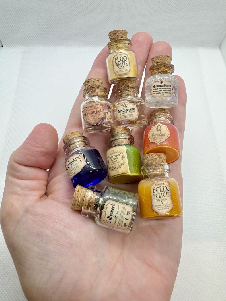 May include: A collection of miniature potion bottles with cork stoppers. The bottles contain various colored liquids and powders, with labels such as "Floo Powder" and "Felix Felicis". The bottles are held in a hand.