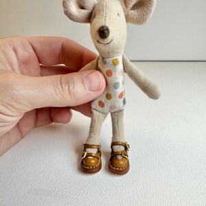 May include: A handmade fabric mouse doll with large, floppy ears and a stitched face. The mouse wears a polka-dot dress and brown leather shoes with gold buckles. The doll is a whimsical, handcrafted item.