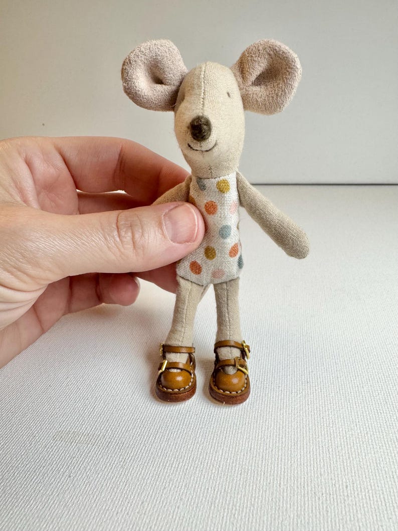 May include: A handmade fabric mouse doll with large, floppy ears and a stitched face. The mouse wears a polka-dot dress and brown leather shoes with gold buckles. The doll is a whimsical, handcrafted item.