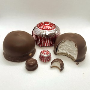May include: A close-up of five chocolate covered marshmallow candies. One candy is partially eaten, revealing the white marshmallow inside. The candies are wrapped in red and white foil with a star logo.