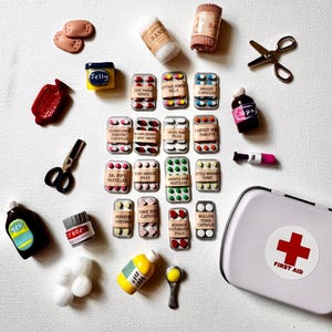 May include: A miniature first aid kit set including a white metal case with a red cross, various blister packs of labeled pills, small bottles, scissors, bandages, and medical supplies. The items feature labels like Tiny Tonsil Tonics, Snoozy Capsules, and Willow Tonic Capsules.