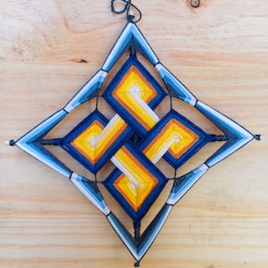 Könnte beinhalten: Ein blauer, gelber und weißer Wandbehang aus Fäden in Form eines Sterns. Der Stern ist aus Garn gefertigt und in ein komplexes Muster gewebt.