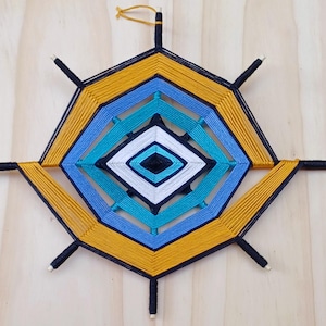 Peut inclure: Un attrape-rêves coloré avec un motif jaune, bleu et turquoise. L'attrape-rêves a huit cordes noires attachées au bord extérieur.