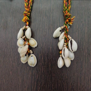 Può includere: Due fili di corda colorata con conchiglie bianche attaccate. Le corde sono legate insieme in alto e le conchiglie pendono a grappolo.