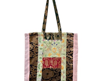 May include: A patchwork tote bag with a variety of patterned fabrics. The bag features a combination of floral, paisley, and solid fabrics in shades of green, red, gold, black, and pink. The handles are green and gold.