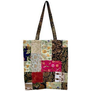 May include: A patchwork tote bag with a variety of fabric patterns and colors. The bag features a mix of floral and geometric designs in shades of gold, green, pink, and blue. The handles are a dark brown with a gold floral pattern.