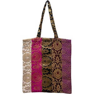 May include: A colorful tote bag with a patchwork design. The bag features vertical panels of various colors and patterns, including gold floral designs on white, pink, black, and purple backgrounds. The handles are black with gold accents.