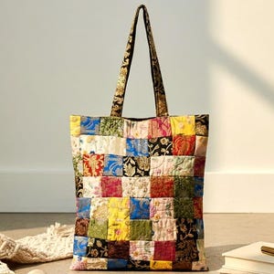 Può includere: Una colorata borsa tote patchwork con quadrati di tessuto nei toni del rosso, giallo, blu e verde. I manici hanno un motivo floreale scuro. La borsa è appoggiata su un pavimento di cemento.