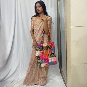 May include: A beige sari with sequin detailing and a patchwork tote bag. The tote bag features a variety of colorful fabric squares in shades of pink, blue, green, and orange. The bag has a matching strap.