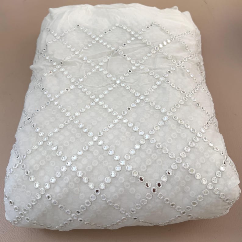 May include: White fabric with a diamond pattern of small, reflective embellishments. The fabric appears soft and slightly translucent, with the embellishments catching the light. The overall effect is delicate and decorative.