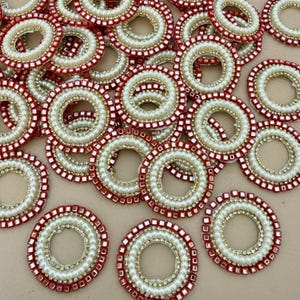 Peut inclure: Une collection d'ornements circulaires décoratifs. Chaque anneau présente une bordure extérieure rouge, un anneau central de perles blanches et un anneau intérieur de perles dorées. Les ornements sont conçus pour les travaux manuels et les projets d'embellissement.