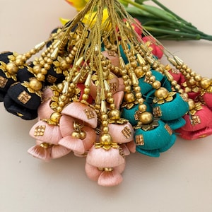 Puede incluir: Una colección de borlas de seda coloridas en varios tonos, incluyendo negro, rosa, turquesa y coral. Cada borla presenta un hilo de cuentas doradas y adornos decorativos. Las borlas están agrupadas, mostrando su intrincado diseño y colores vibrantes.