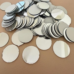 Può includere: Una collezione di piccoli pezzi rotondi di vetro a specchio. I dischi argentati hanno superfici riflettenti, creando un aspetto luminoso e brillante. Questi elementi decorativi sono sparsi su una superficie neutra.