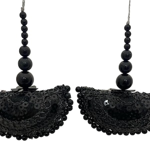 Peut inclure: Paire de boucles d'oreilles noires perlées. Chaque boucle d'oreille présente un motif en demi-cercle avec des paillettes noires et une bordure en dentelle. Une chaîne de perles noires graduées est suspendue au-dessus du demi-cercle.