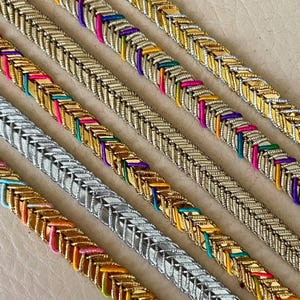 May include: Close-up of several colorful, braided bracelets. The bracelets are made of metallic links and feature vibrant accents of pink, yellow, blue, and green. The bracelets are arranged diagonally, showcasing their intricate design and color variations.