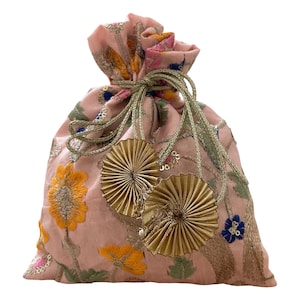 May include: A pink drawstring pouch with intricate floral embroidery in yellow, blue, and green. The bag features gold-colored tassels and a matching drawstring closure. The pouch is likely made of a soft, textured fabric.