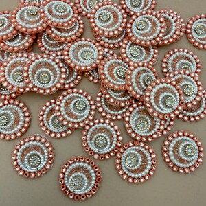 May include: A collection of coral and white beaded embellishments. Each circular piece features a spiral design with a central jewel and is surrounded by a border of small beads. These decorative elements are ideal for craft projects.
