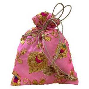 Op de afbeelding: Een roze satijnen zakje met gouden borduursels en pailletten. De trekkoordtas heeft een pauwenveerontwerp en gouden kwastjes. De tas is aan de bovenkant vastgebonden met een gouden koord.