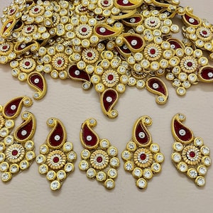 Op de afbeelding: Goudkleurige sieraden met ingewikkelde bloemen- en paisley-ontwerpen. De stukken hebben rode accenten en zijn versierd met heldere, sprankelende stenen. De sieraden zijn gerangschikt op een lichtgekleurd oppervlak, waarbij de details worden getoond.