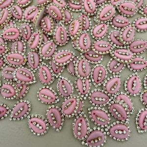 Può includere: Una collezione di abbellimenti rosa a forma ovale con bordo dorato e strass trasparenti. Ogni abbellimento ha una fila centrale di tre strass. Questi pezzi decorativi sono adatti a vari progetti artigianali.