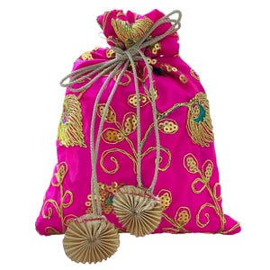 Peut inclure: Un sac à cordon fuchsia vif avec broderies et sequins dorés. Le motif floral est rehaussé de détails turquoise et dorés. Le sac a une fermeture à cordon dorée et deux pompons dorés décoratifs.