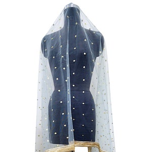May include: A sheer, light blue veil with gold sequin embellishments. The veil is draped over a black mannequin, showcasing its delicate texture and design. The bottom edge features a gold trim.