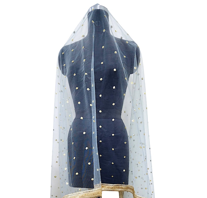 May include: A sheer, light blue veil with gold sequin embellishments. The veil is draped over a black mannequin, showcasing its delicate texture and design. The bottom edge features a gold trim.