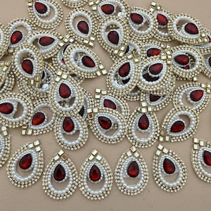 Puede incluir: Colección de adornos ornamentados en forma de lágrima. Cada pieza presenta una joya central en forma de pera, de color rojo intenso, rodeada de perlas de imitación blancas y un borde dorado con tachuelas cuadradas. Ideal para manualidades.